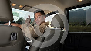 Happy young handsome man sitting inside car and showing thumbs up. Travel and active lifestyle concept