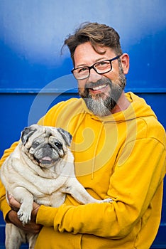 Happy young handsome man smile and hold his own old dog pug - cheerful people and animals lifestyle - caucasian male with beard