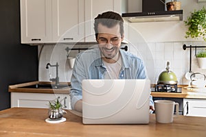 Happy young handsome man using computer in kitchen.