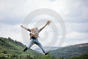 Happy young hiker man jumps with a backpack in the mountains