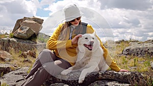 Happy young hiker woman cares, strokes lovely dog sitting on wild area outdoors