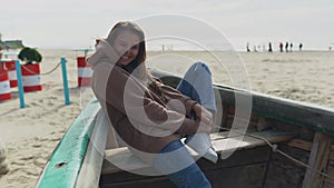 Happy young hipster woman have fun in old boat on beach with white sand and laughing. Autumn, seaside, outdoor, vacation