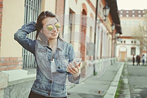 Happy young hipster woman walking on the street, using her smartphone