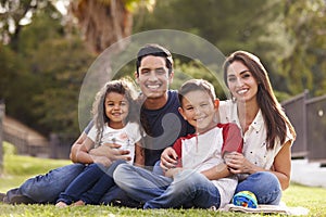 Happy young Hispanic family sitting the on grass in the park smiling to camera, close up