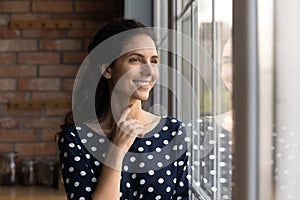 Happy young hispanic female looking through big window dreaming indoors