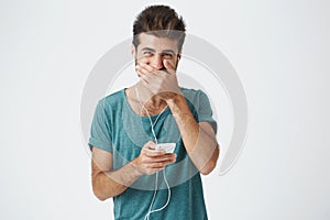 Happy young hispanic stylish man wearing fashionable blue t shirt, smiling and looking to camera, covering mouth with