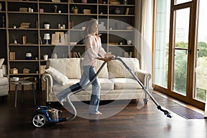 Happy young homeowner cleaning parquet floor with vacuum cleaner