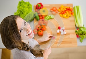 Happy young housewife cutting fresh vegetables