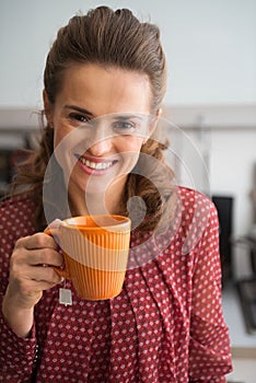 Happy young housewife drinking tea in kitchen