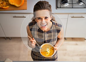 Happy young housewife eating pumpkin soup