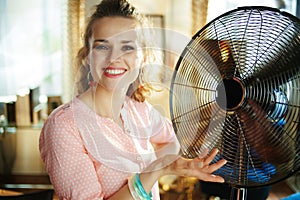 Happy young housewife showing metallic floor standing fan