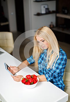 Happy young housewife with tablet pc eating fruits