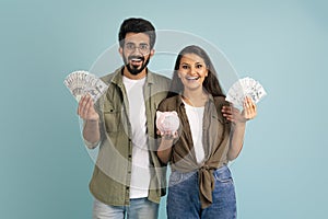 Happy young indian couple holding cash and piggybank