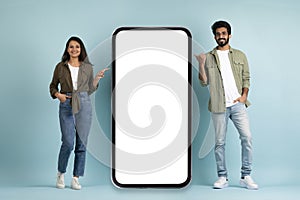 Happy young indian couple pointing at big cell phone, mockup