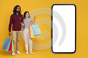Happy young indian couple shopping together on yellow, mobile app