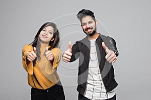 Happy young indian couple showing thumbs up and looking at camera isolated over gray background