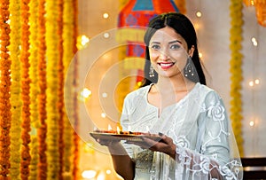 Happy young indian girl with diya lamps on plate during diwali festival celebration looking camera - concept of photo