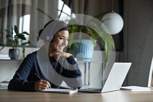 Happy young indian girl with headphones looking at laptop screen.