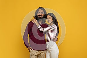 Happy young indian man and woman embracing on yellow background