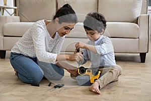 Happy young indian mother fixing toy car with little son.