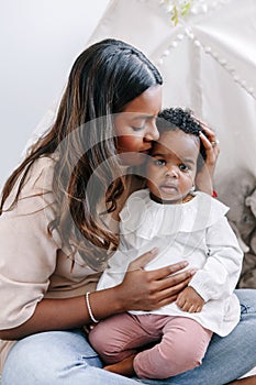 Happy young Indian mother playing kissing mixed race black baby girl daughter. Family mixed race people mom and kid together