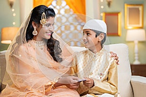 happy young indian muslim mother gifting or giving money to son during ramadan festival - concept of savings, finance