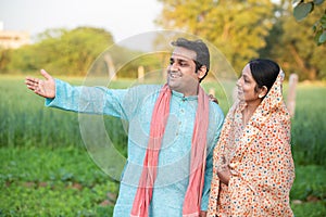 Happy young indian rural farmer couple in agricultural field looking at each other laughing