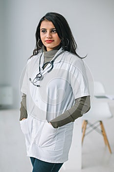 Happy young indian woman doctor wearing white medical coat and stethoscope looking at camera. Smiling female physician