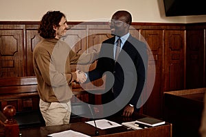 Happy young intercultural male suspect and his attorney shaking hands photo