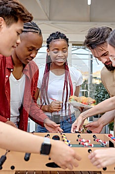 happy young interracial students playing table soccer, at barbecue outdoor party