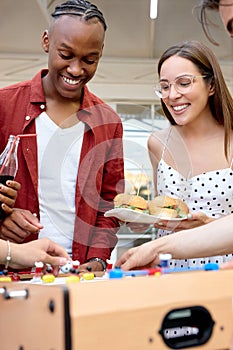 happy young interracial students playing table soccer, at barbecue outdoor party