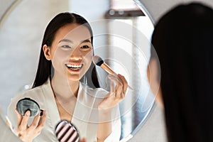 Happy young japanese woman applying blush and smiling