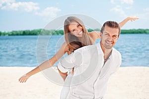 Happy young joyful couple having beach fun piggybacking laughing together during summer holidays vacation on the beach. Beautiful