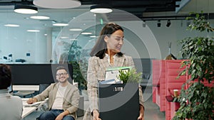 Happy young lady former employee quitting job leaving office room with box of things