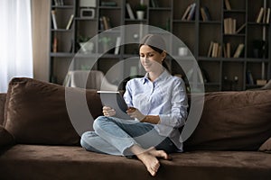 Happy young lady rest on comfy sofa holding digital tablet