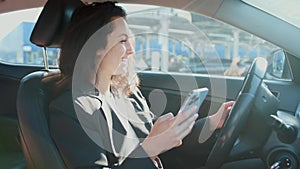 Happy young lady typing message on the smartphone, driving the car. Slow motion