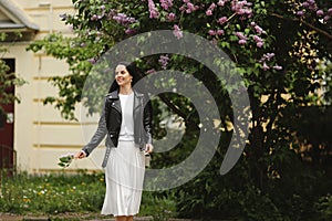 Happy young lady walking on the street near the bloomy lilac tree on the summer day photo