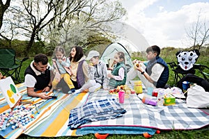 Happy young large family with four children having fun and enjoying outdoor on picnic blanket at garden spring park, relaxation