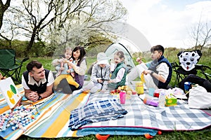 Happy young large family with four children having fun and enjoying outdoor on picnic blanket at garden spring park, relaxation