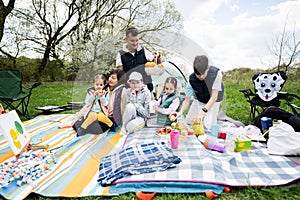 Happy young large family with four children having fun and enjoying outdoor on picnic blanket at garden spring park, relaxation