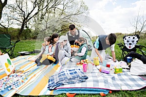 Happy young large family with four children having fun and enjoying outdoor on picnic blanket at garden spring park, relaxation