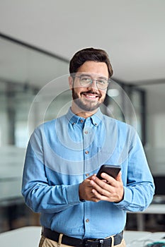 Happy young latin business man holding smartphone in office. Vertical portrait.