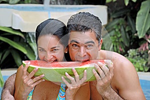 Happy young latin couple eating watermelon in the pool