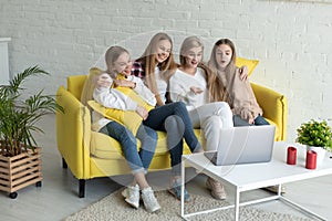 Happy young lesbian couple with daughters in casual clothes sitting together on yellow sofa at home