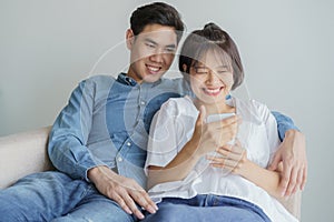 Happy young love Asian couple sitting on couch at home, looking at mobile phone, Young asian people are using smartphone
