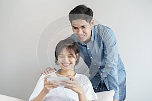 Happy young love asian couple sitting on  couch at home, looking at mobile phone, Young asian people are using smartphone