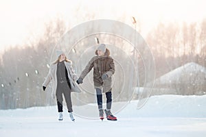 Happy young love couple hold hands, skate on rink, it snows in winter. Concept vacations outdoor activities