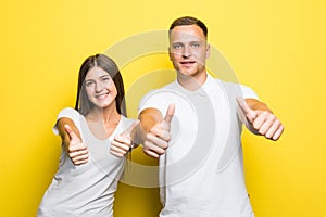 Happy young lovely couple showing thumbs up and looking at the camera over yellow backgroun