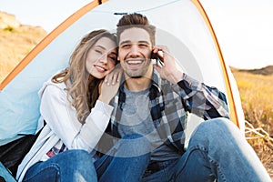 Happy young loving couple outside in free alternative vacation camping talking by mobile phone