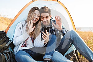 Happy young loving couple outside in free alternative vacation camping talking by mobile phone